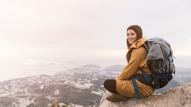 Free: Smiling young woman sitting on the top of mountain with her backpack  Free Photo 