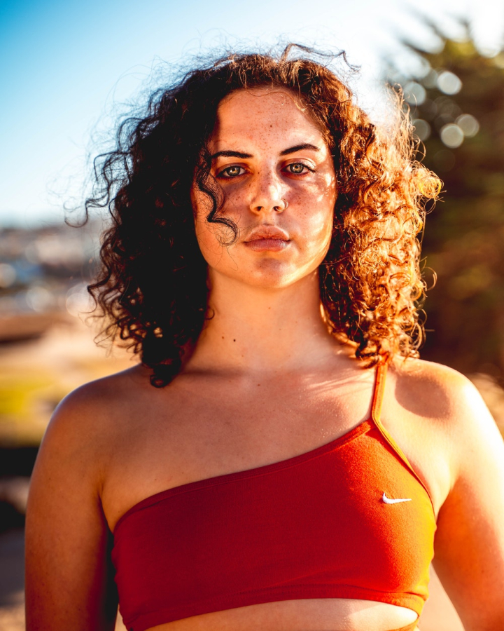 curly hair,daylight,facial expression,female,gaze,looking,serious,skin,sports bra,staring,sunny,woman