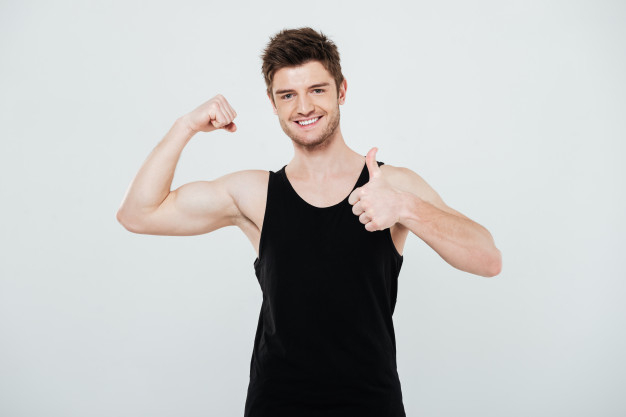 Free: Smiling young sportsman flexing biceps and showing thumbs up