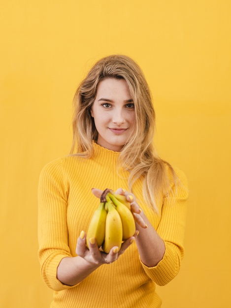 medium shot,yellow outfit,expressive,medium,posing,outfit,pose,blonde,vertical,pretty,shot,adult,portrait,beautiful,young,female,model,banana,yellow background,yellow,fruit,woman,background