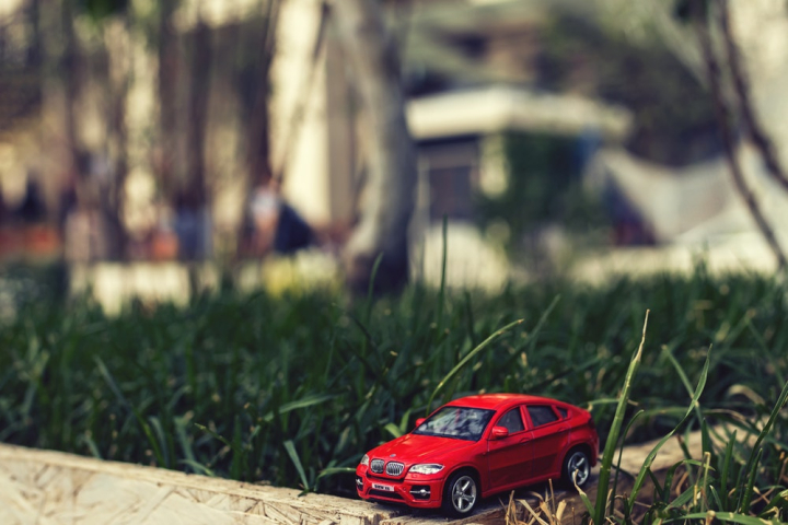 automobile,blurred background,bmw,car,close-up,daylight,focus,front,grass,outdoors,red,toy,toy car,traffic,vehicle,wheels