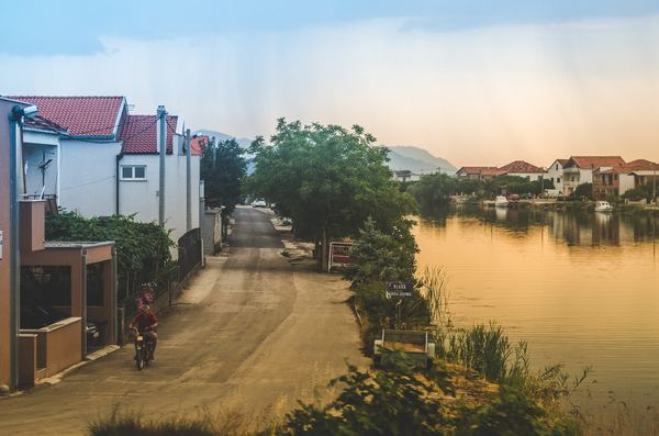 woman,girl,city,cityscape,city,building,property,house,architecture,village,village by the sea,lake,eater,village street,sunset,sunset light,river,water,house,suburb,road