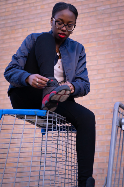 adult,african descent,air jordan,city,crate,eyeglasses,eyewear,fashion,jacket,looking,outdoors,people,person,portrait,sitting,street,tying shoes,urban,wear,woman,young
