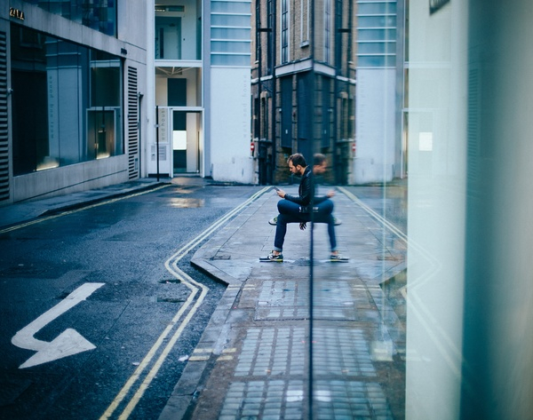 building,architecture,road,street,sidewalk,people,guy,man,sitting,waiting,texting,wall,reflection