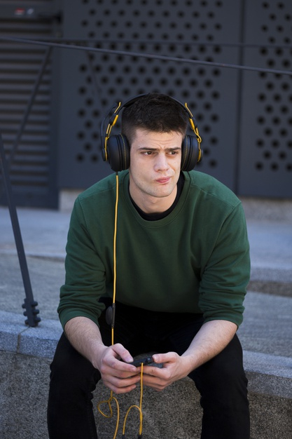 frowning,pensive,melancholy,frown,thoughtful,jumper,handsome,leisure,outdoors,listening,adult,depression,rest,look,sit,guy,break,male,activity,device,expression,gadget,urban,relax,sad,headphones,street,yellow,black,face,man,phone,green,music