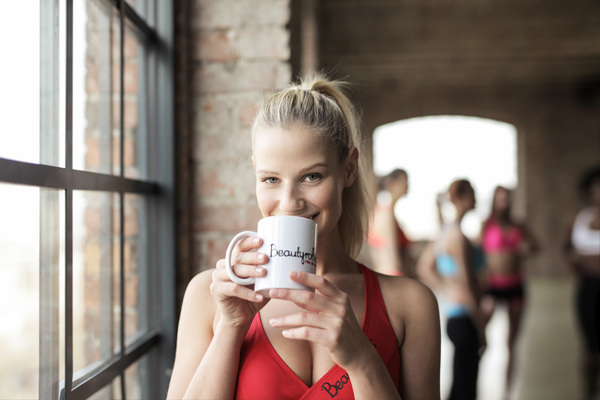 20-25 year old,adult,fit,indoors,red,relaxing,sport,young,blonde,body,calm,caucasian,coffee,female,fitness,gym,hair,health,lifestyle,mug,relaxation,smile,sports bra,sportswear,strength,strong,toned,training,weight,wellness,woman,workout