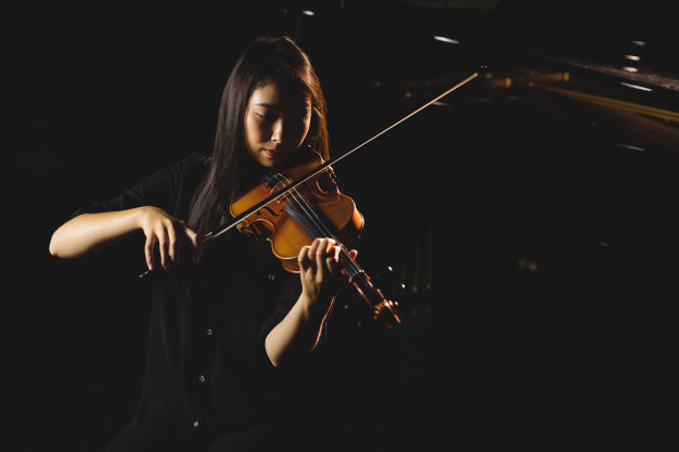 attentive,casual clothing,indoors,focused,illuminated,performer,perform,concentration,expertise,casual,acoustic,leisure,playing,holding,instrument,hobbies,skill,profession,musician,musical,performance,musical instrument,sitting,artist,violin,professional,learn,clothing,learning,bow,music