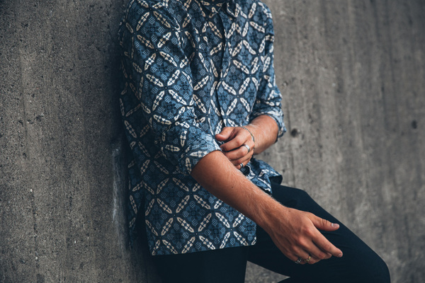 adult,blue,clothing,grey,hand,hat,one person,portrait,standing,caucasian,concrete wall,fashion,fashionable,fingers,glass,hands,leaning on wall,lifestyle,long hair,male,man,outside,patterned shirt,person,rings,style,stylish,wrist watch