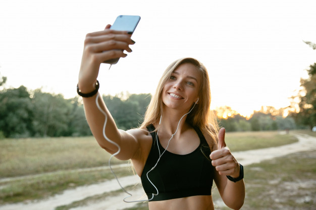 tree,music,summer,phone,nature,sport,fitness,mobile,happy,smartphone,person,park,mobile phone,headphones,selfie,thumbs up,female,cellphone,young,beautiful