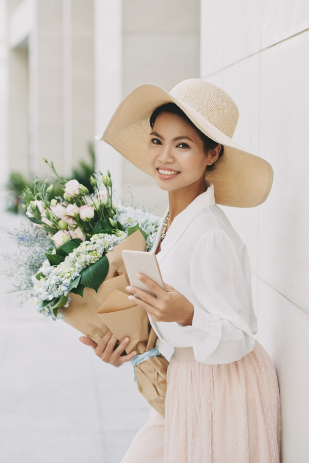 toothy,fashionable,charming,blooming,bunch,vietnamese,florist,smiling,pretty,beautiful,gadget,asian,application,bouquet,romantic,lady,street,hat,communication,smartphone,happy,woman,city,flower