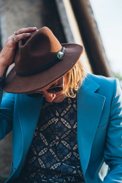adult,blue,clothing,grey,hand,hat,jacket,one person,portrait,sitting,standing,sunglasses,sunlight,brown hat,caucasian,coat,concrete walls,fashion,fashionable,glass,lifestyle,long hair,male,man,outside,patterned shirt,person,rings,style,stylish,turquoise blue jacket