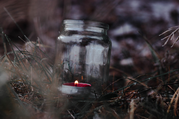 blurred background,candle,close-up,colors,flame,glass,grass,jar,lighted,outdoors