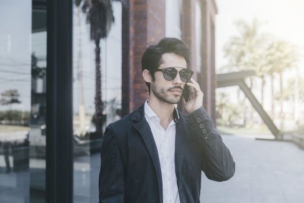 technology,building,fashion,phone,man,wall,tropical,smartphone,person,glass,success,communication,call,sunglasses,talking,young,jacket,cool,gadget,expression