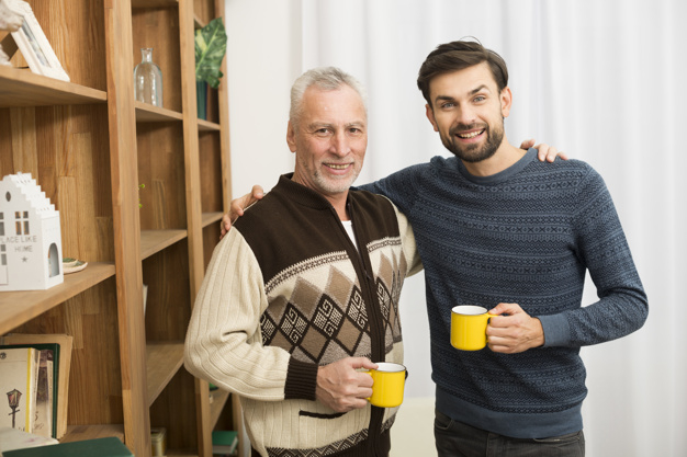 camera,man,happy,room,white,drink,cup,curtain,father,mug,relax,care,together,young,bookshelf,elderly,positive,male,beverage,senior,guy,rest,parent,horizontal,smiling,looking,cups,wear,comfort,leisure,hugging,casual,son,aged,indoors,embracing,at,fatherhood,looking at camera,multigenerational,with
