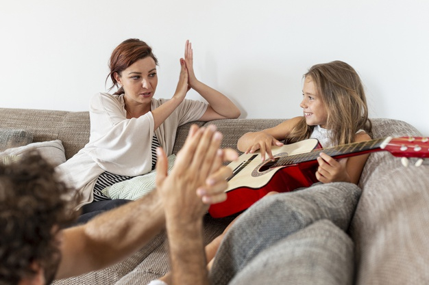 indoors,clapping,husband,togetherness,daughter,wife,living,playing,horizontal,male,lifestyle,sitting,parents,dad,together,female,sofa,father,mom,guitar,room,mother,home,girl,man,woman,family,house