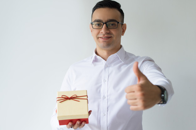 recommending,approving,showing,front,looking,smiling,celebrating,horizontal,formal,adult,holding,guy,male,positive,christmas bow,greeting,thumb,day,up,portrait,holding hands,christmas box,year,boxing day,manager,young,surprise,thumbs up,studio,christmas gift,worker,business man,new,businessman,present,person,glasses,event,gift card,holiday,shirt,bow,promotion,anniversary,gift box,box,xmas,man,camera,hand,gift,party,new year,birthday,business,christmas,business card