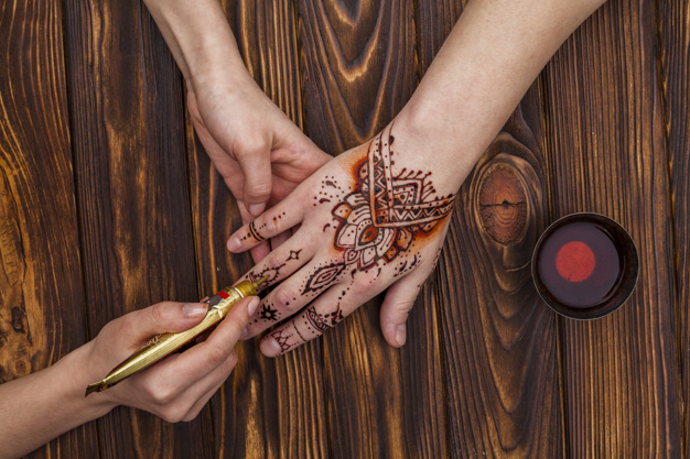 unrecognizable,applying,faceless,near,body part,making,dye,womans,part,mehndi,crop,anonymous,horizontal,master,holding,beverage,ornate,top view,top,beauty woman,hand painted,holding hands,beautiful,view,tea cup,asian,henna,artist,tool,wooden background,professional,traditional,wood table,culture,skin,brown background,hand drawing,wooden,mug,brown,pattern background,nature background,natural,ethnic,cup,body,drawing,process,desk,drink,decoration,wood background,person,tea,tattoo,art,paint,table,woman,ornament,hand,pattern,background