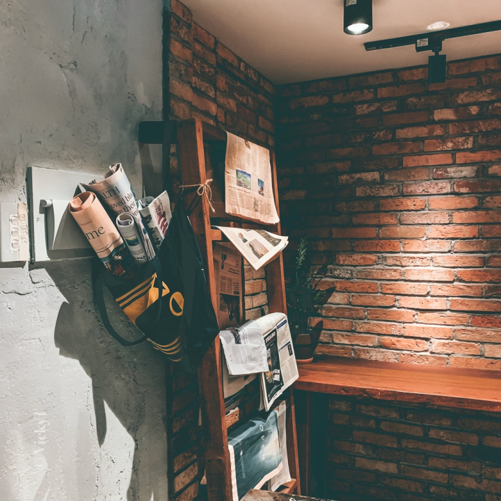 art,bag,brick wall,building,lights,newspaper,newspaper stand,rack,room,wall