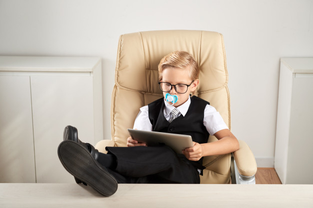pretend,caucasian,using,soother,dummy,pacifier,ceo,executive,feet,device,sitting,boss,reading,play,fun,chair,mouth,tablet,desk,boy,job,businessman,glasses,child,kid,work,office,baby,business