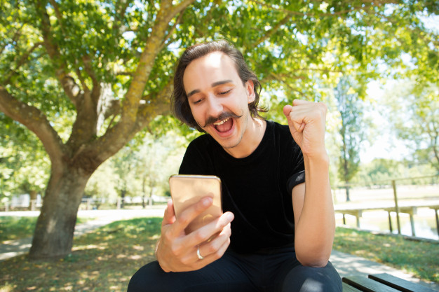overjoyed,rejoicing,getting,handlebar,making,shouting,casual,handsome,excited,outdoors,smiling,celebrating,winning,adult,holding,curly,guy,gesture,joy,male,bench,cell,portrait,sitting,smart,good,young,cellphone,screen,moustache,message,model,open,reading,mouth,news,park,winner,success,person,human,shirt,mobile,man,phone