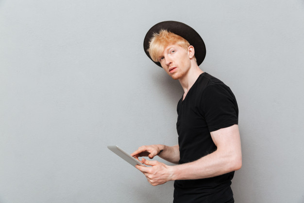 caucasian,attractive,blonde,casual,handsome,chatting,standing,looking,adult,guy,pocket,male,arm,sms,portrait,cool,young,relax,youth,hat,tablet,person,human,student,man,computer,people