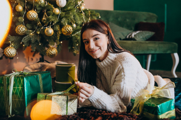 Free: Young woman by christmas tree unpacking gifts Free Photo