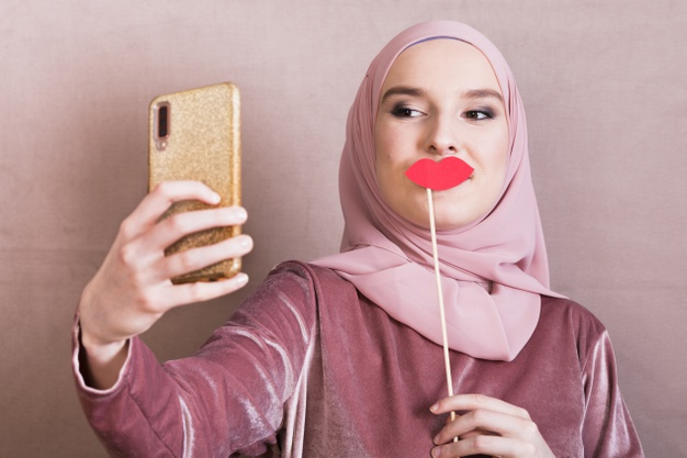 headscarf,pout,taking,covered,mobilephone,front,prop,smiling,tradition,pretty,one,elegance,adult,wireless,religious,arabian,hijab,stick,beautiful,asian,arab,scarf,young,cellphone,female,traditional,culture,electronic,electric,selfie,studio,lady,muslim,tech,lips,ethnic,person,backdrop,smartphone,human,happy,smile,beauty,pink,camera,woman,islamic,technology,people,background
