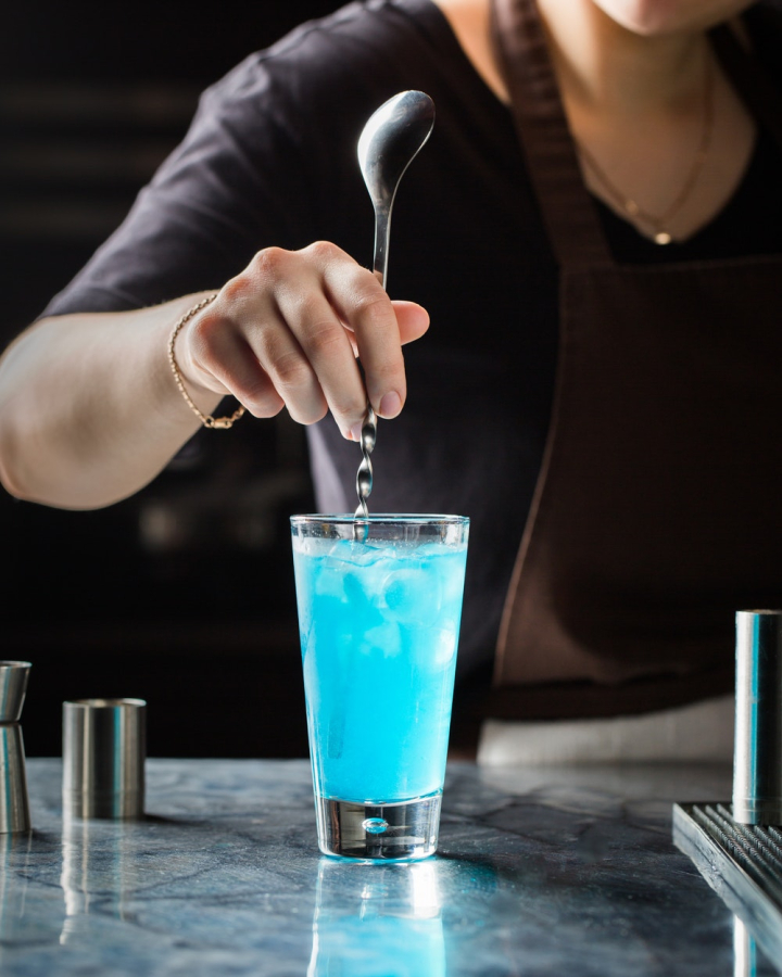 alcohol,alcoholic beverage,bar,bartender,beverage,blue,close-up,cocktail,cocktail glass,cold,cool,drink,drinking glass,gin,glass,ice,indoors,liquid,liquor,mix,mixing,refreshing,spoon,tasty,vodka,woman