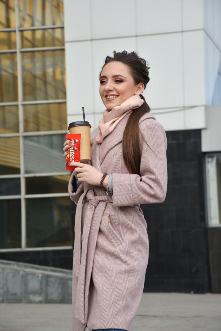 beautiful woman,beverage,brunette,candy packet,coffee to go,enjoyment,eye makeup,facial expression,holding,make up,outerwear,photoshoot,posing,pretty,smiling,standing,woman