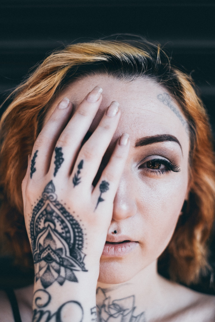 body art,covered,covering,face,facial expression,female,fingers,hair,hairstyle,hand,looking,skin,tattooed,tattoos,woman