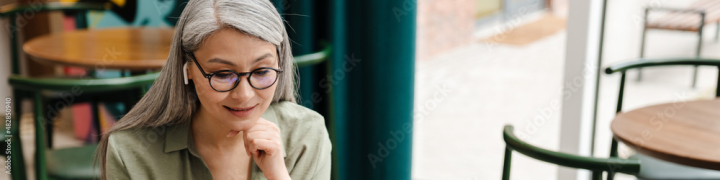 panorama,panoramic,cropped,woman,adult,mature,cafes,asian,earphones,to sit,laptop,music,grey,use,computer,listen,long hair,day,smile,cyberspace,1,table,people,indoor,gesture,adobestock