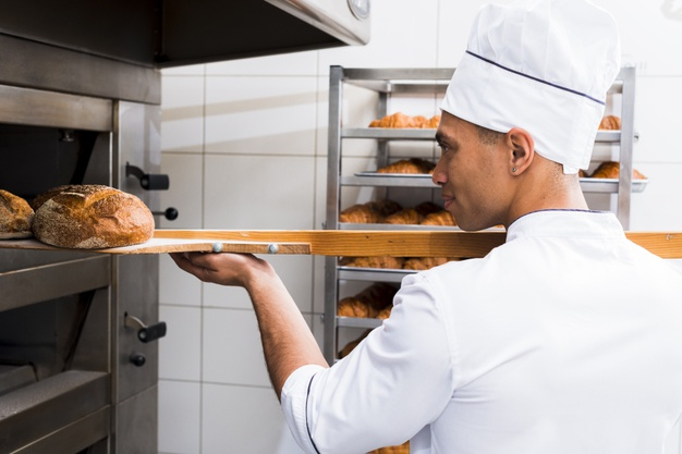 Baker taking out freshly baked bread from the oven of a bakery stock photo