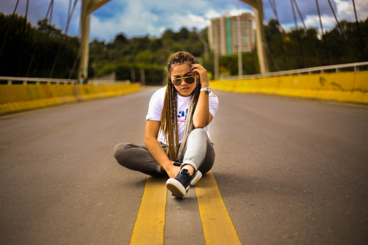 Young attractive hipster girl hitchhiking sits on the highway fence and  holds a bouquet of lilac flowers. She is dressed in top and jeans.  Backlight p Stock Photo - Alamy
