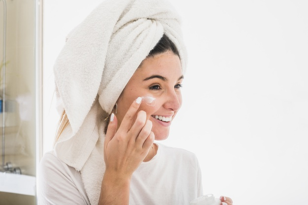 Woman Wrapped with Bath Towels, Applying Cream on her Face Stock