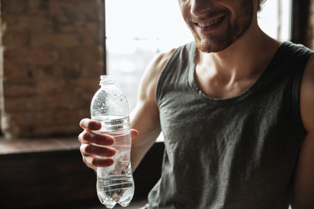 Muscular man holding his water bottle and resting from workout