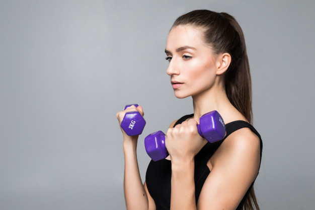 Young fitness woman is in the gym near wall with dumbbells in