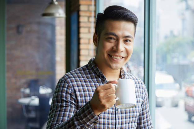 casualwear,toothy,sipping,vietnamese,cheerful,handsome,smiling,shot,holding,chest,guy,drinking,up,asian,young,mug,window,cafe,tea,man,coffee