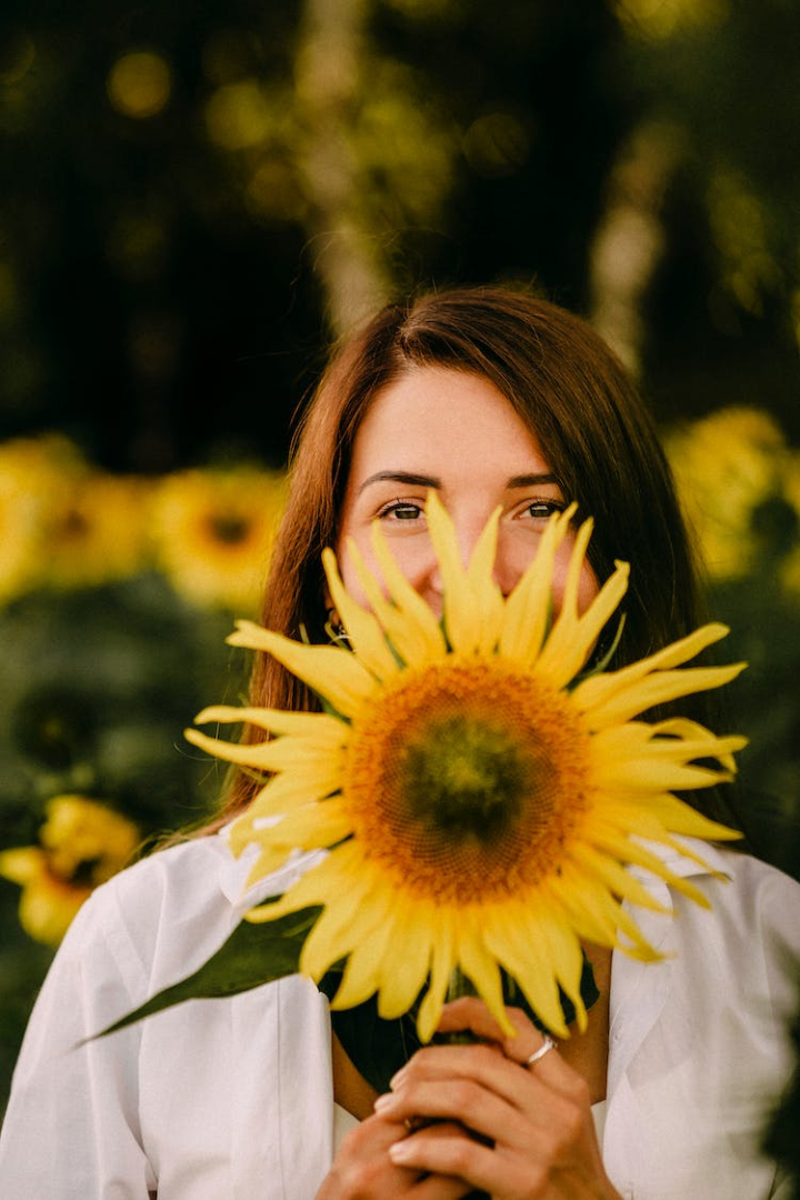 bloom,close-up,flora,holding,person,sunflower,vertical shot,woman,yellow flower