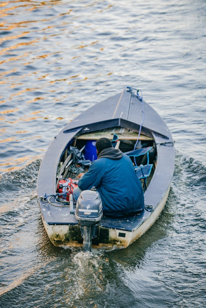 blue jacket,boat,body of water,canal,creek,high angle shot,man,person,river,sitting,solo,vertical shot,watercraft