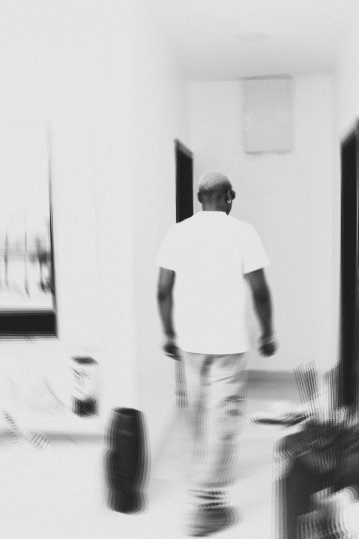 back view,black and white,blurred,man,room,vertical shot,walking,white t-shirt