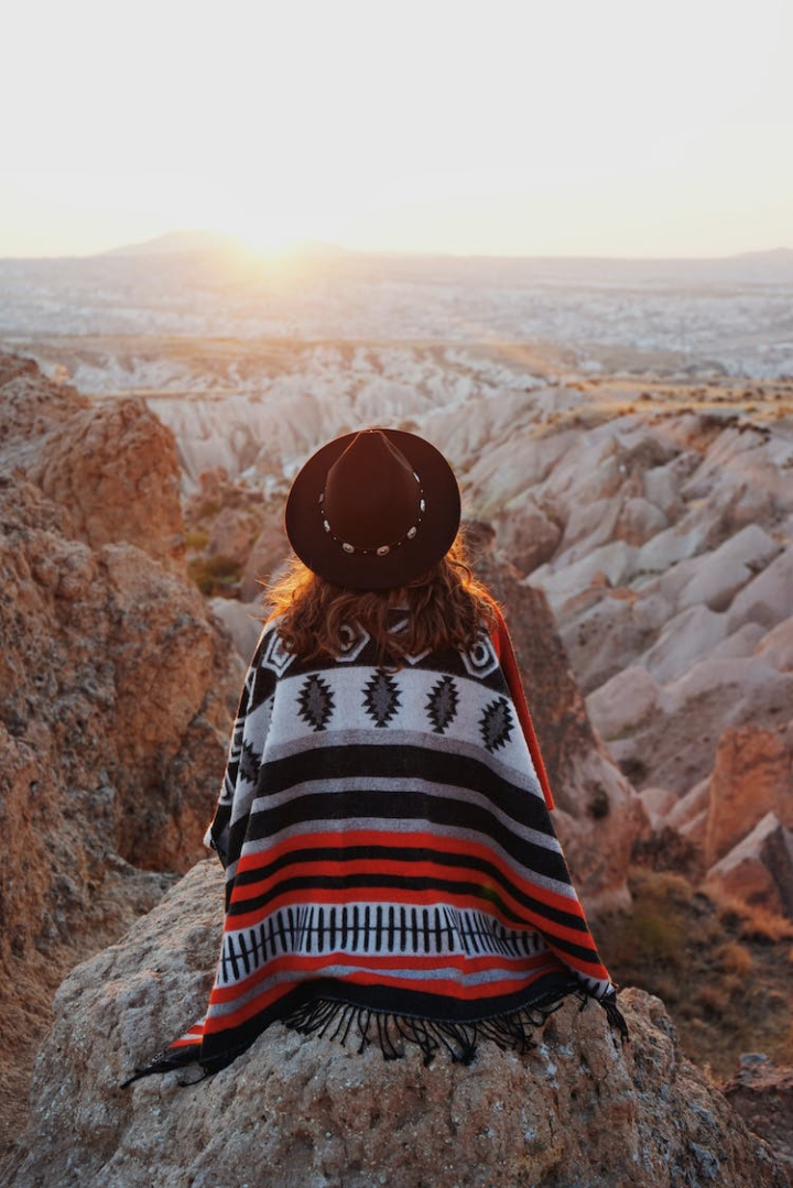 back view,cappadocia,mountain range,mountains,sitting,sunlight,sunset,turkey,valley,vertical shot,woman