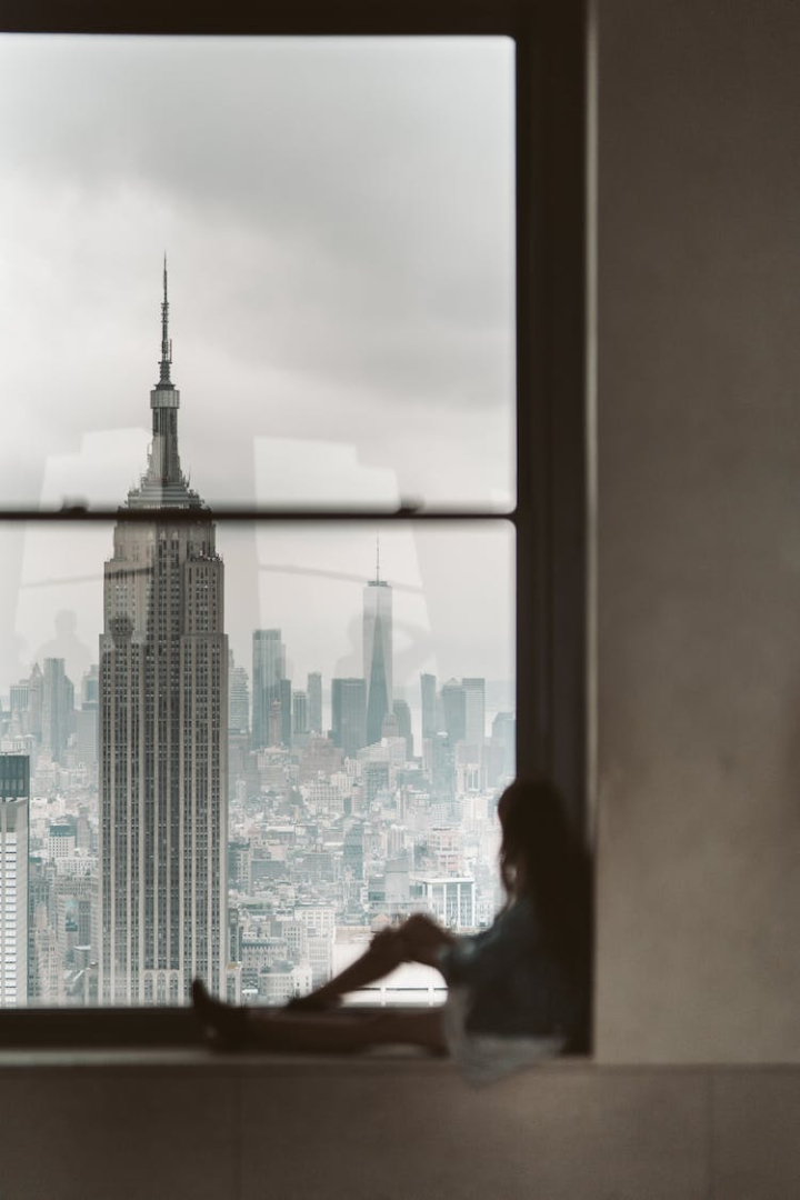architecture,building,city,city view,dawn,dusk,empire state building,looking out,new york,new york city,nyc,office buildings,sitting,window,windows,woman
