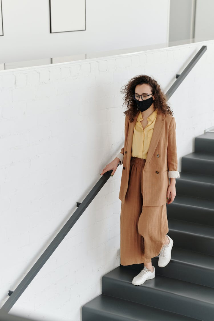 2019 ncov,awareness,brunette,business woman,coronavirus,covid 19,curly hair,elegant,eyeglasses,face mask,fashion,fashionable,mask,metal railing,model,modern,moving down,outbreak,pandemic,person,prevention,protection,stairs,stay safe,step,virus,walking,wear,woman,young