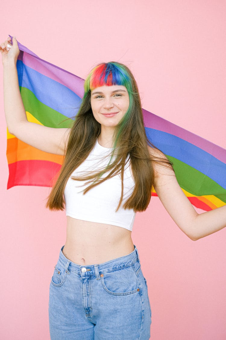 colored hair,cute,gay pride,gay pride flag,girl,hair,hairstyle,holding,lgbt,lgbt pride,lgbtq,looking at camera,model,pink background,pretty,rainbow,rainbow bangs,rainbow flag,smile,smiling,woman,young woman