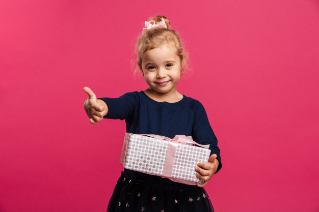 innocence,adorable,innocent,showing,blond,attractive,little,confident,small,blonde,childhood,looking,smiling,pretty,holding,look,thumb,expression,young,female,youth,finger,child,kid,happy,celebration,cute,girl,box,gift