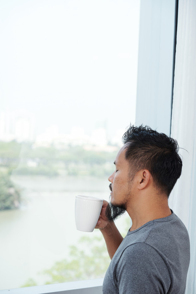 asian and indian ethnicities,ethnicities,contemplating,enjoying,smelling,early,caffeine,closed eyes,wellbeing,casual,front,leisure,aroma,standing,adult,guy,closed,drinking,male,lifestyle,asian,morning,mug,thinking,cup,eyes,window,indian,tea,home,man,coffee