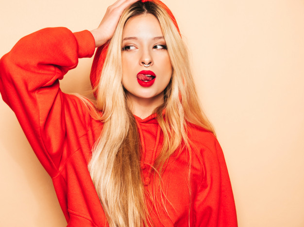 Free: Portrait of young beautiful hipster bad girl in trendy red hoodie and  earring in her nose. positive model shows tongue Free Photo 