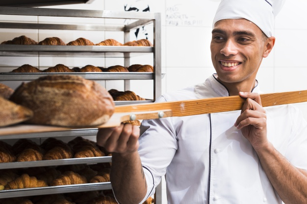 Baker taking out freshly baked bread from the oven of a bakery stock photo