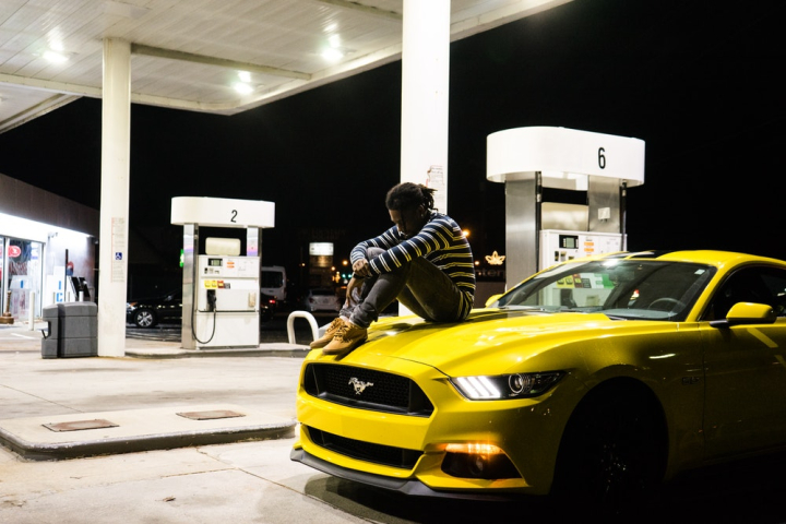 automotive,car,car hood,casual wear,ford mustang,gas station,looking down,man,muscle car,parked,photoshoot,posing,sitting,vehicle,yellow