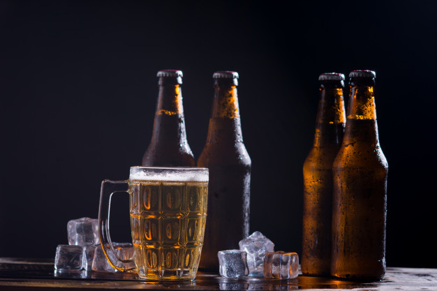 Cold beer with foam in a mug, on a wooden table and a dark background with